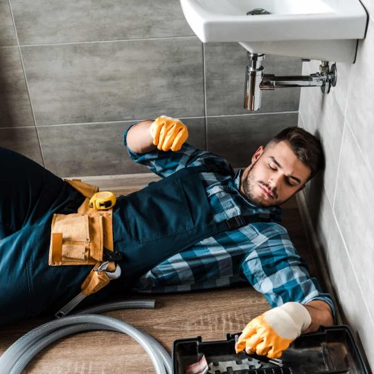 bearded handyman lying on floor near toolbox in bathroom